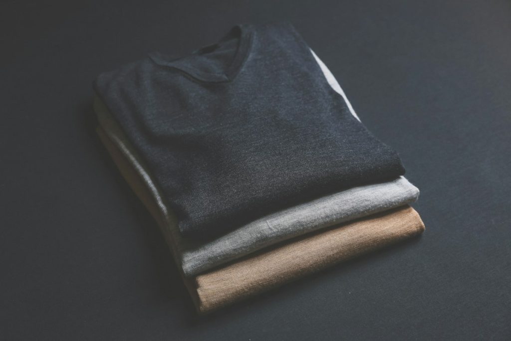 Folded black, grey and brown T-shirts on a dark surface