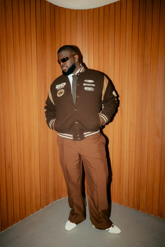 Model in a brown varsity jacket and brown trousers